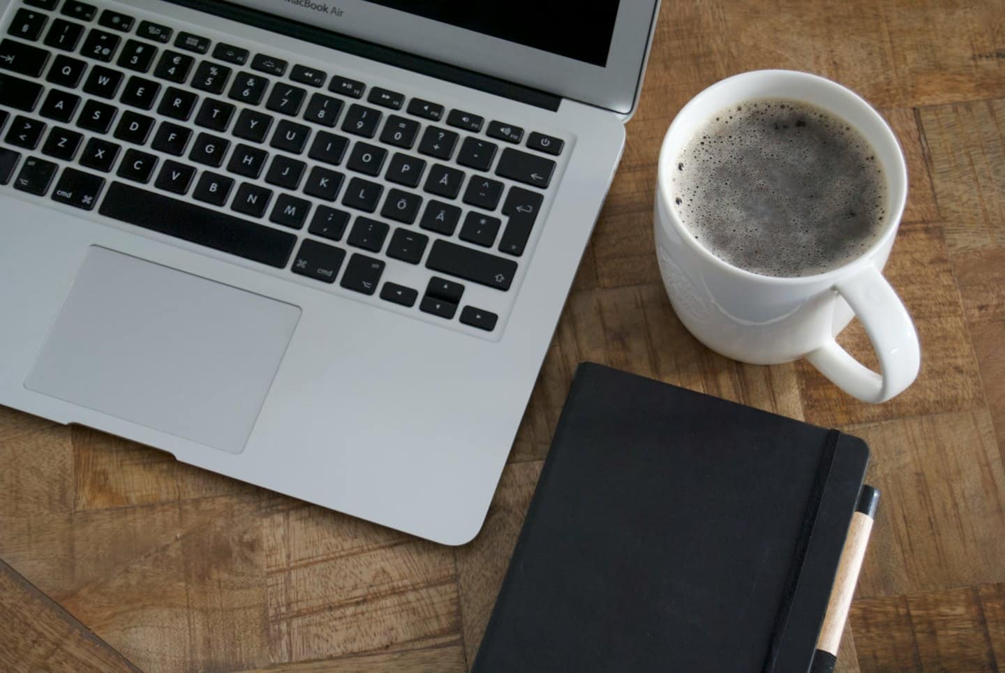 Laptop, notatnik i kawa na drewnianym biurku.